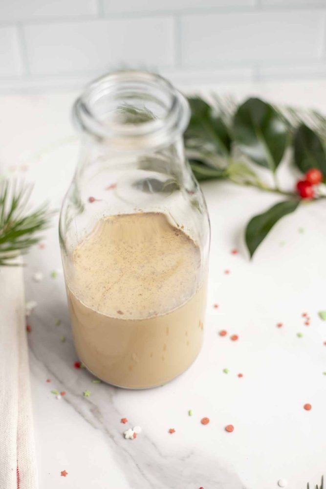 Homemade gingerbread creamer in a glass jar on a white marble countertop with holly in the background