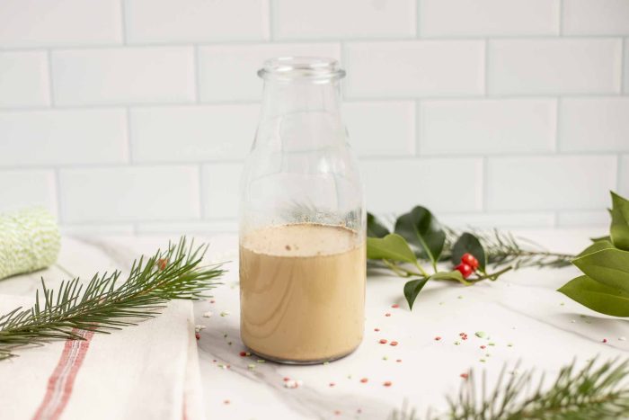 gingerbread coffee creamer in a glass milk jar on a marble countertop surrounded by greenery and holly.