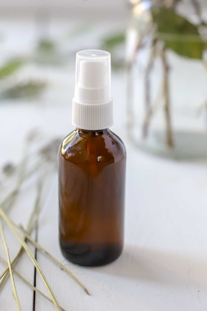 close up picture of homemade face toner in an amber bottle on a white countertop with dried florals surrounding the bottle.