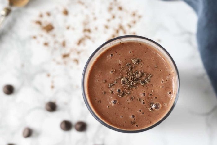 close up overhead photo of a chocolate cauliflower smoothie topped with chocolate. chocolate chips and cocoa powder surrounds the smoothie