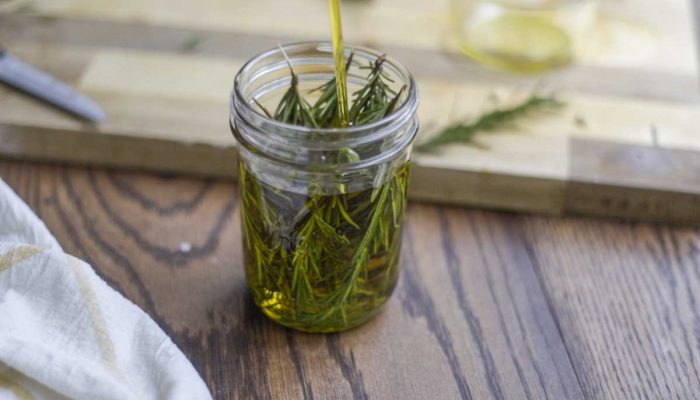 olive oil poured rosemary in a mason jar on a wood countertop