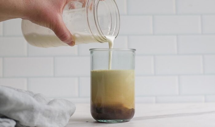 pouring cold foam on top of coffee in a glass