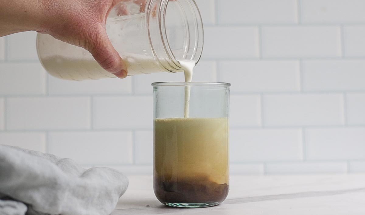 pouring cold foam on top of coffee in a glass.