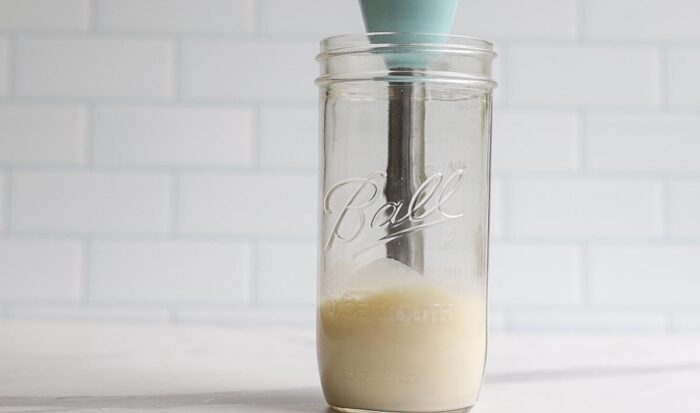 milk being frothed with an immersion blender in a tall mason jar
