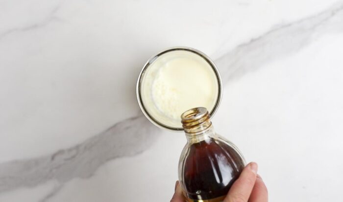 vanilla extract being added to a jar with milk on a marble countertop