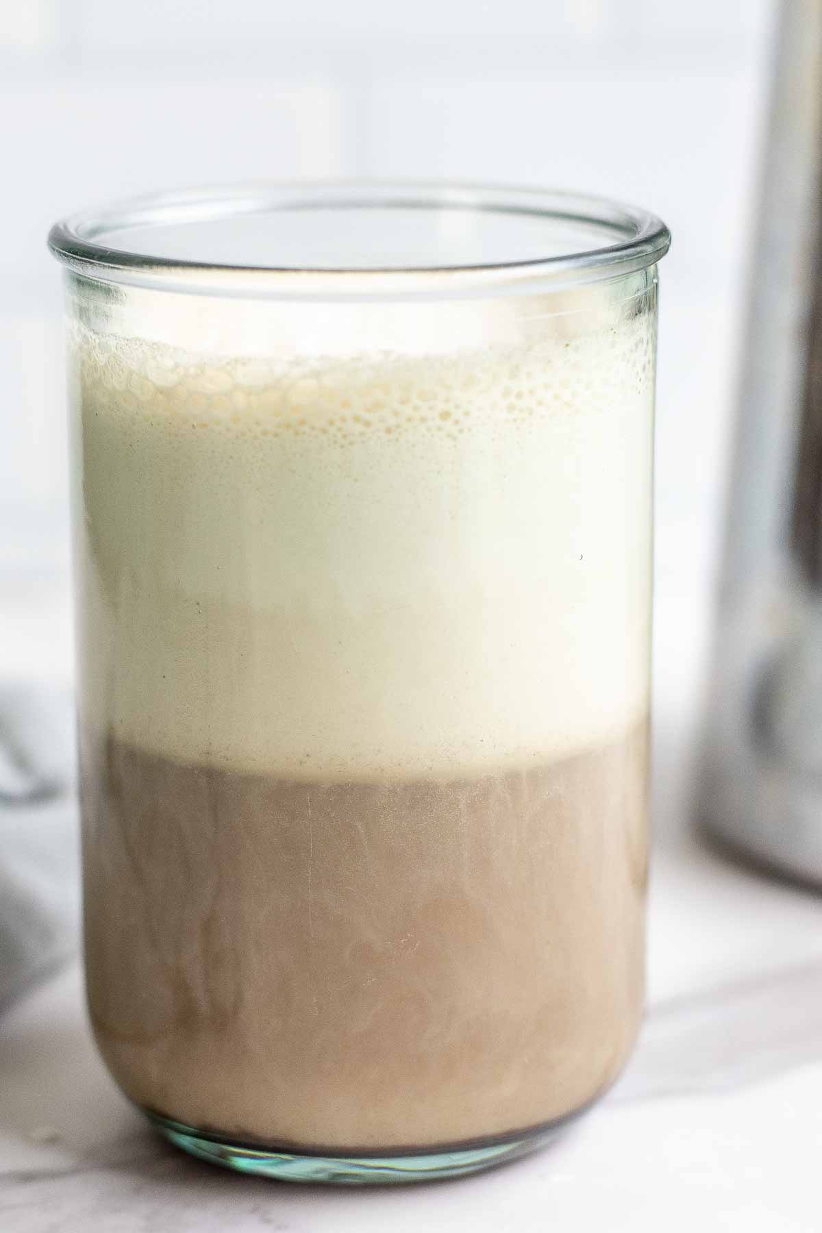 close up photo of coffee topped with cold foam in a glass with a French press in the background.