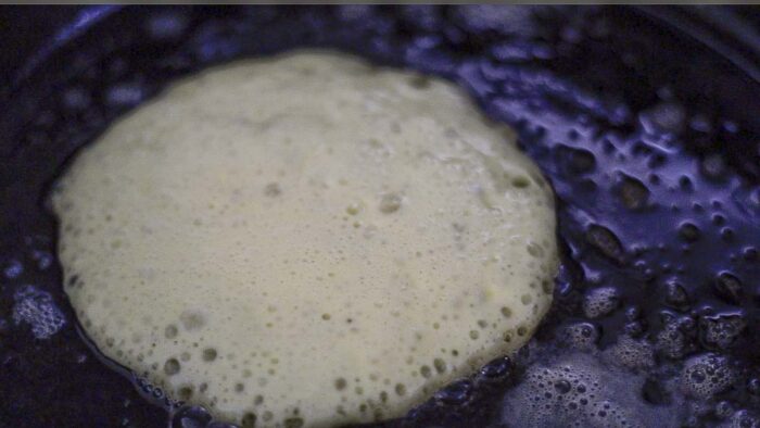 close up picture of a pancake cooking on a cast iron skillet.