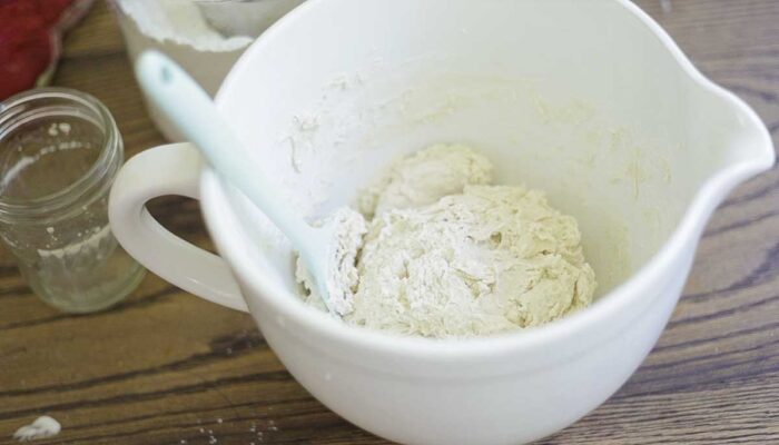 bread dough in a white stand mixer bowl with teal spatula