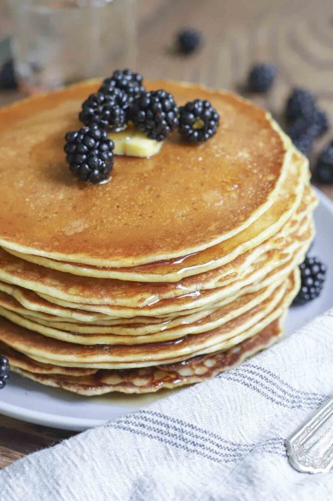 blackberries and butter topping a stack of sourdough discard pancakes on a gray plate with a blue and white stripped towel to the right