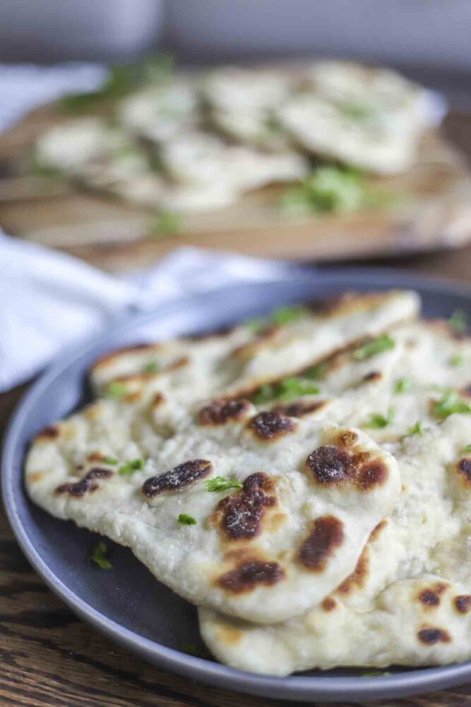 sourdough flatbread piled on a dark gray plate with a cutting board of more flatbreads in the background