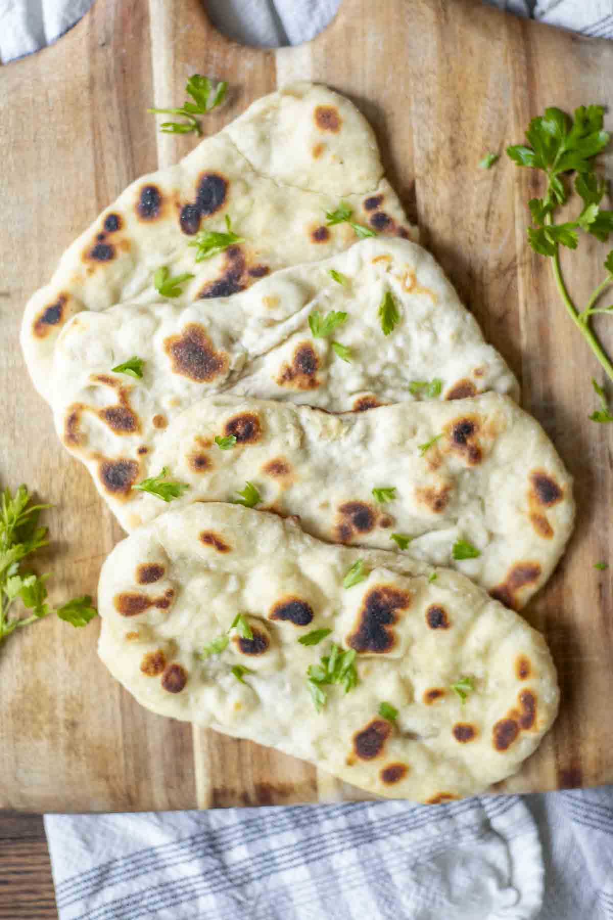 four sourdough flatbreads arranged on a wood cutting board with fresh herbs. The cutting board rests on a blue and white towel