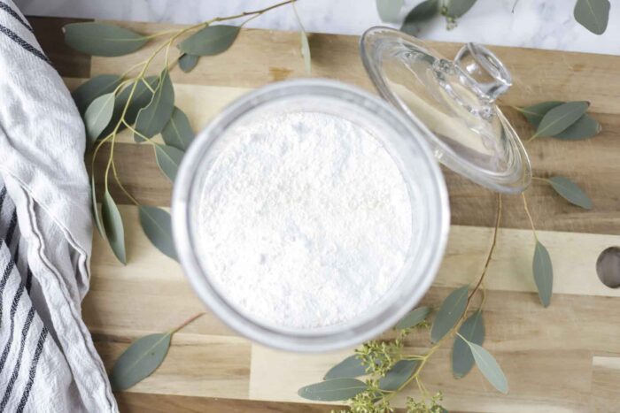 overhead photo of homemade laundry detergent in a glass jar on a wood cutting board with eucalyptus leaves spread around.
