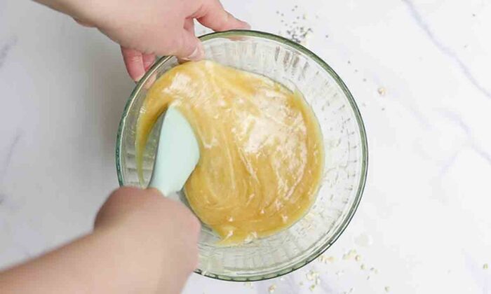 sourdough starter, honey, and oil in a glass bowl getting mixed together with a silicon spatula