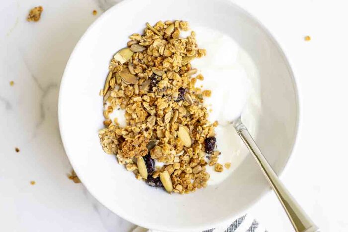 overhead photo of sourdough granola on top of yogurt in a white bowl with a spoon.