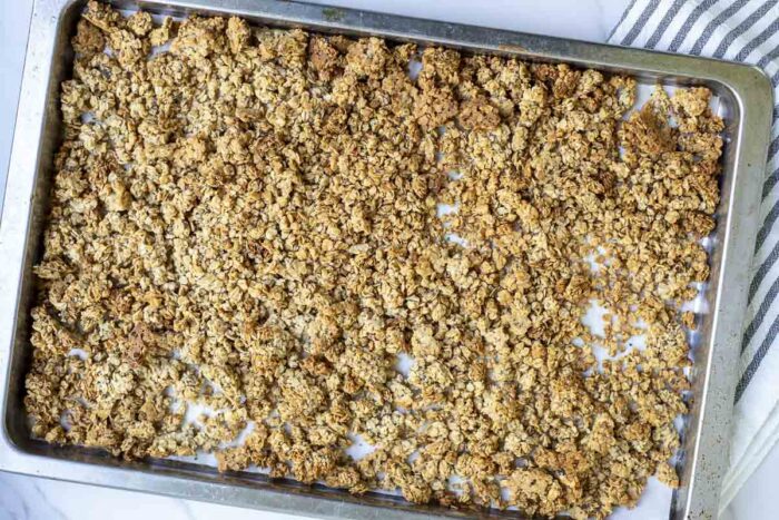 homemade sourdough granola straight out of the oven on a parchment lined baking sheet.