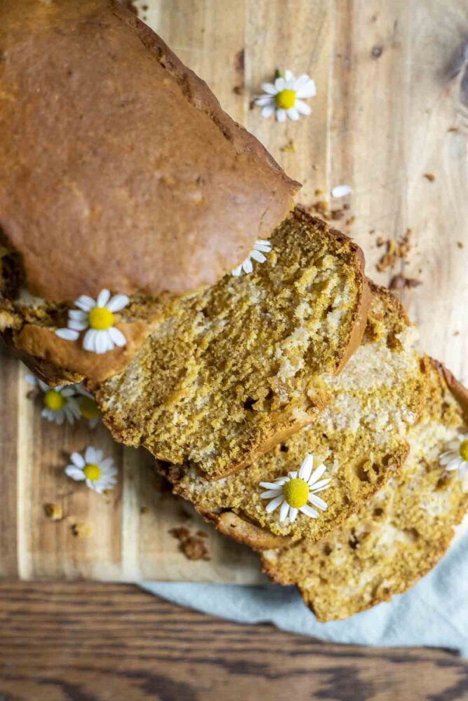 loaf of sourdough pumpkin bread with half the loaf sliced on a cutting board. Chamomile flowers are dispersed throughout