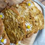 slices of pumpkin sourdough bread topped with chamomile flowers on a wood cutting board