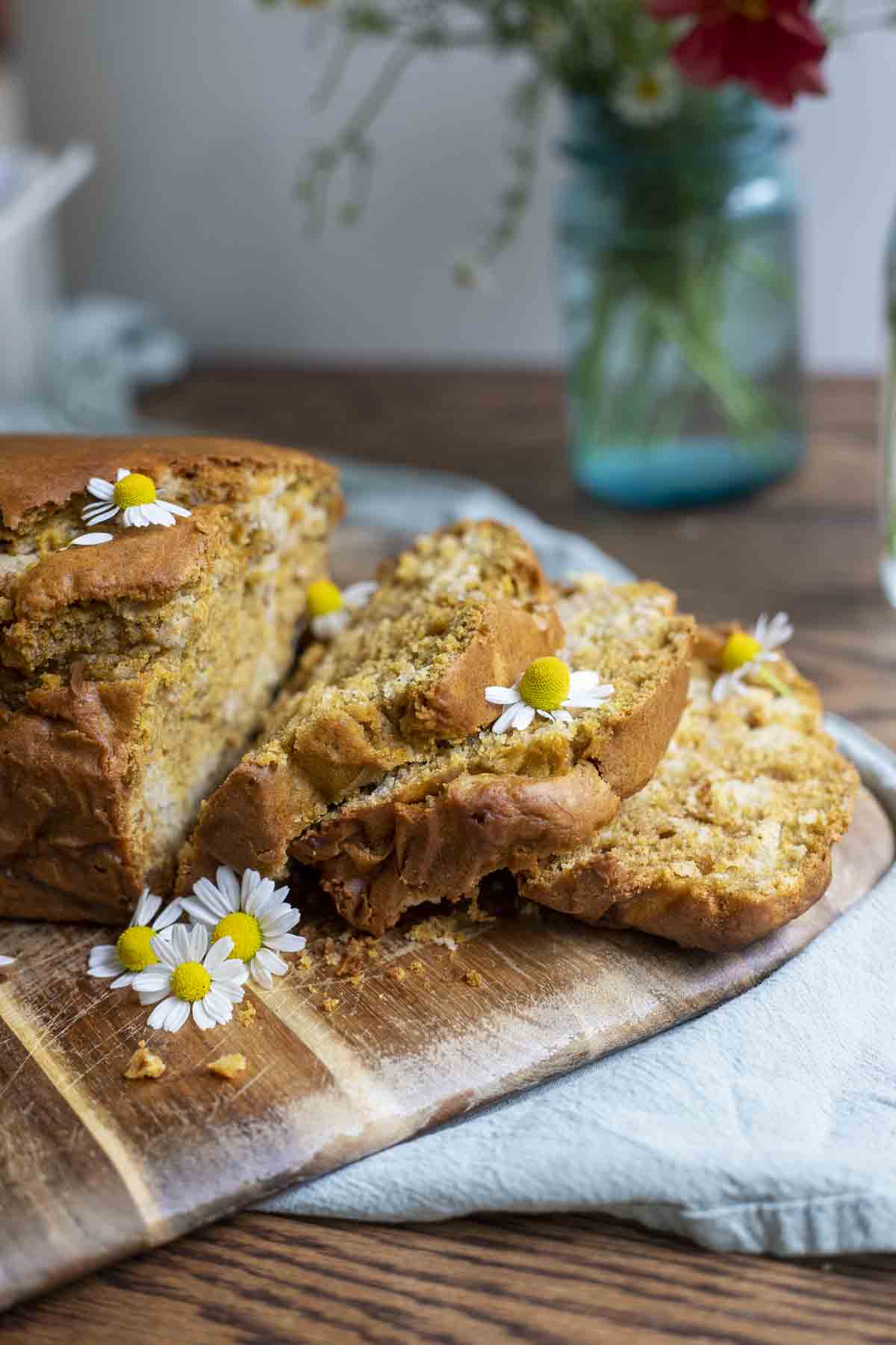 side of pumpkin sourdough bread sliced up on a wood cutting board on a green napkin with a blue jar of flowers in the background