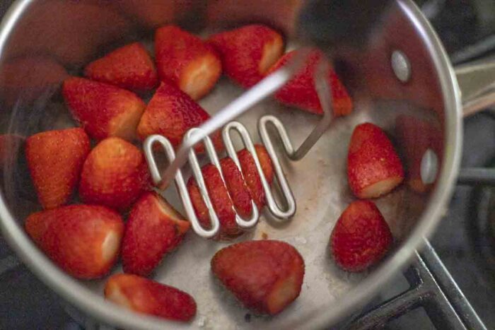 potato masher mashing strawberries in a saucepan