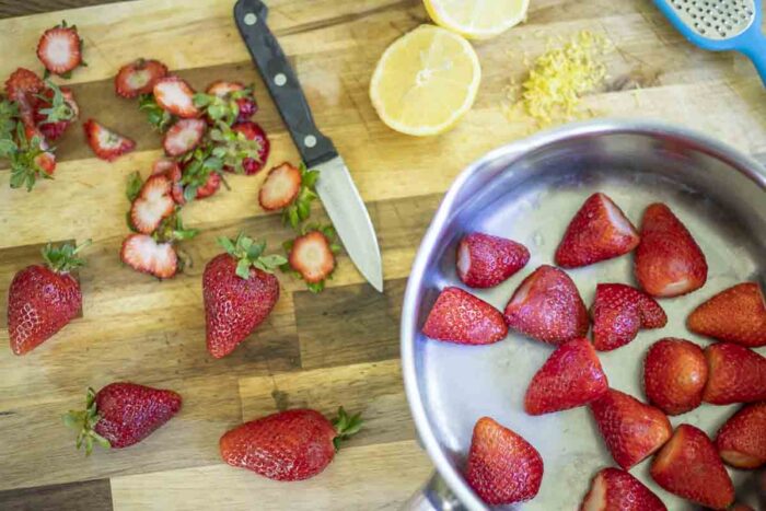 strawberries with greens cut off in a saucepan on a cutting board. 