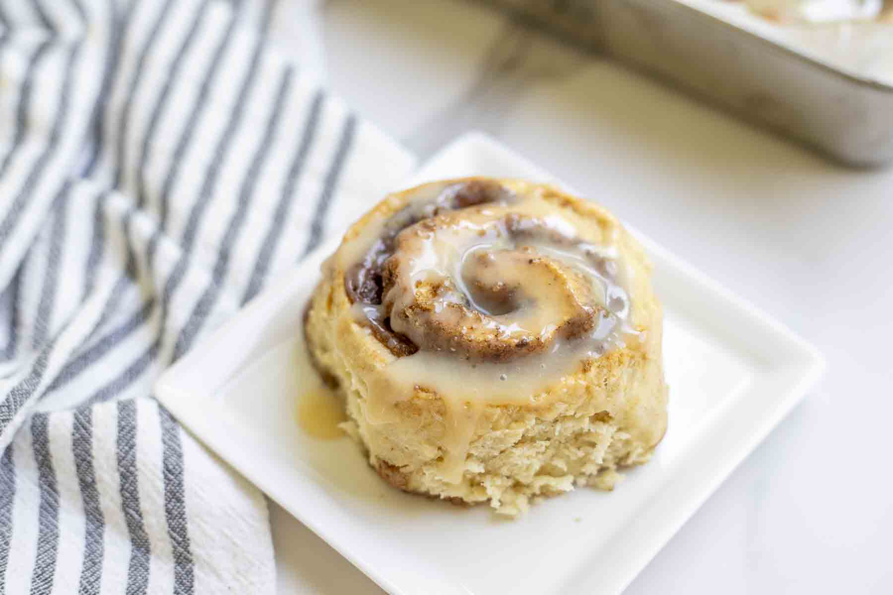 sourdough cinnamon roll on a white plate with a black and white stripped towel