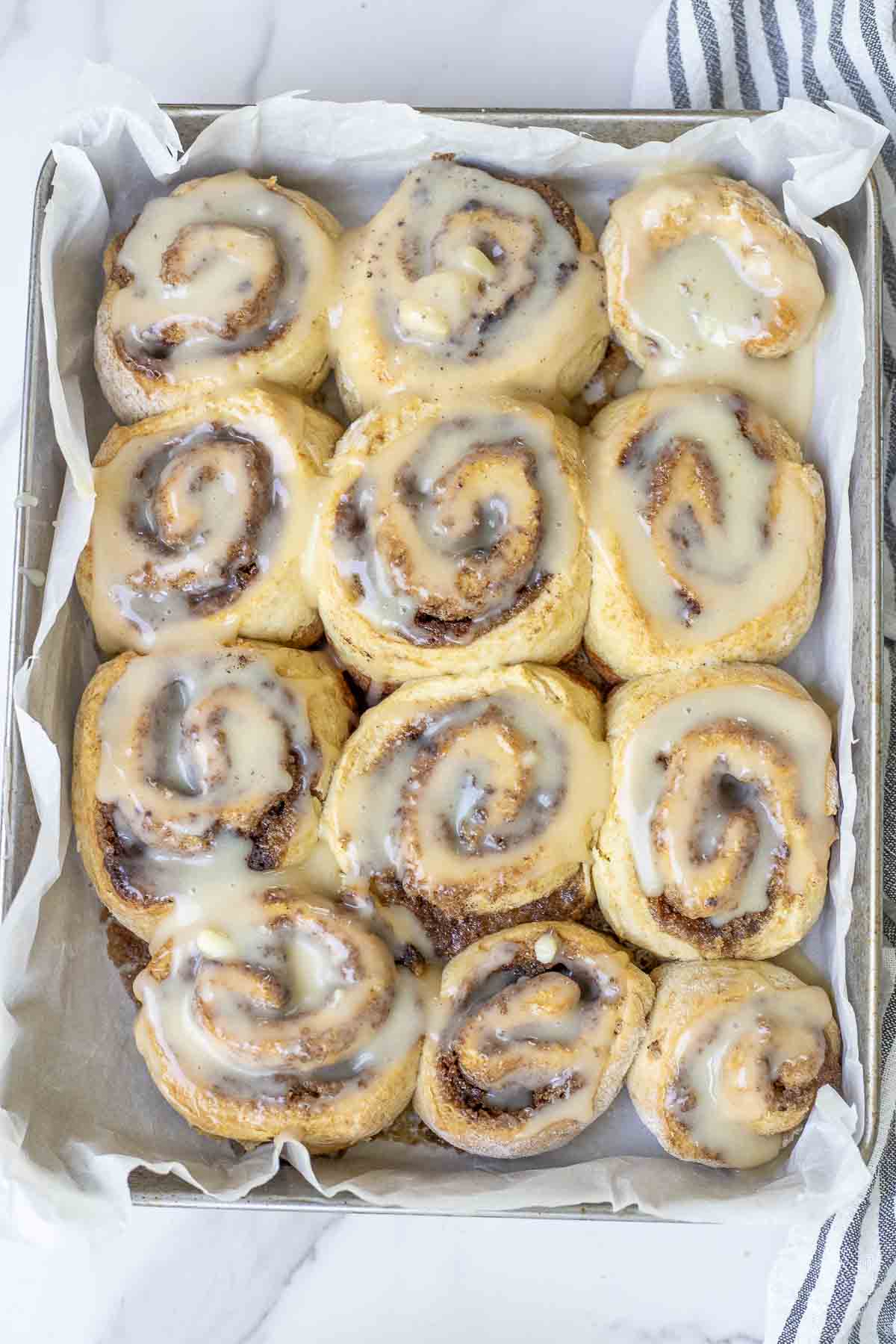 A pan of sourdough discard cinnamon roll-on a marble countertop with a black and white stripped towel