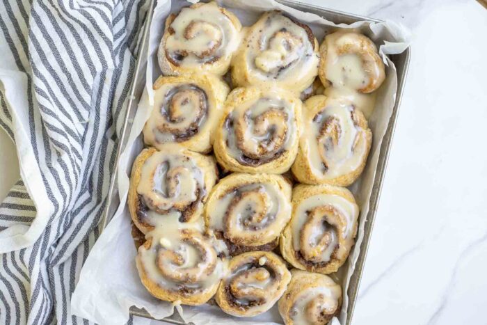 overhead photo of a pan of sourdough cinnamon rolls topped with frosting on a white and black stripped towel 