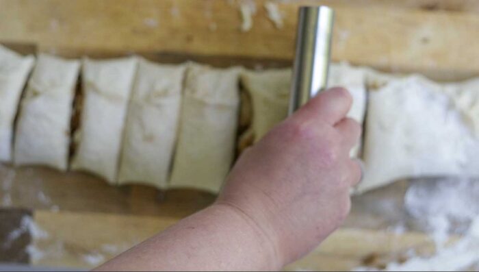 cutting cinnamon roll dough with a bench scraper on a wood cutting board