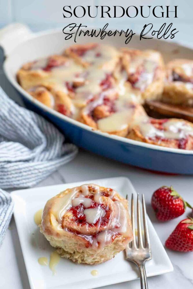 A sourdough strawberry roll on a white plate with a fork. A blue baking dish with more rolls is in the background