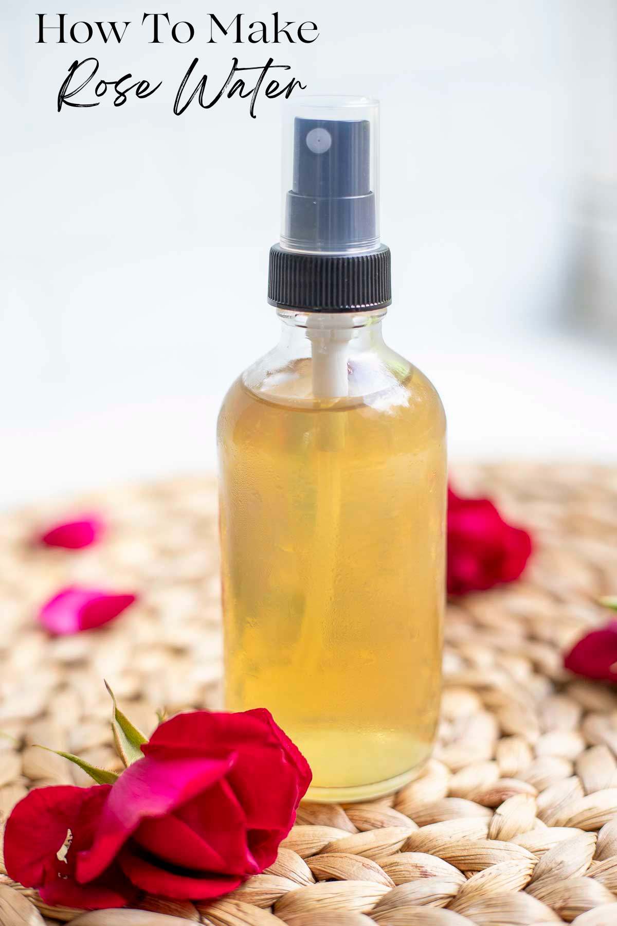 a small glass spray bottle with rose water on a woven place mat with rose petals on top.