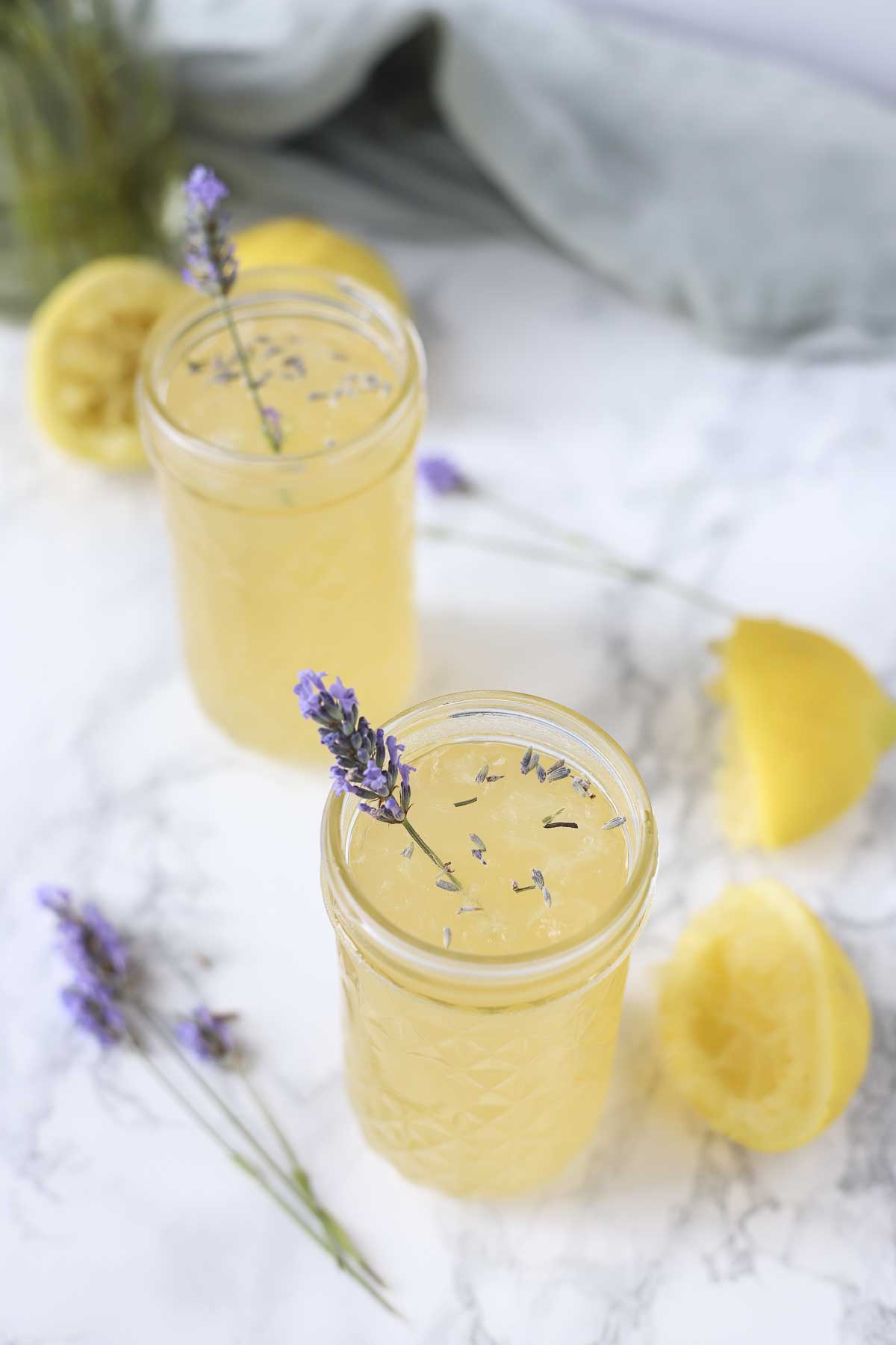 2 glasses of lavender lemonade with lemons ad fresh lavender around it