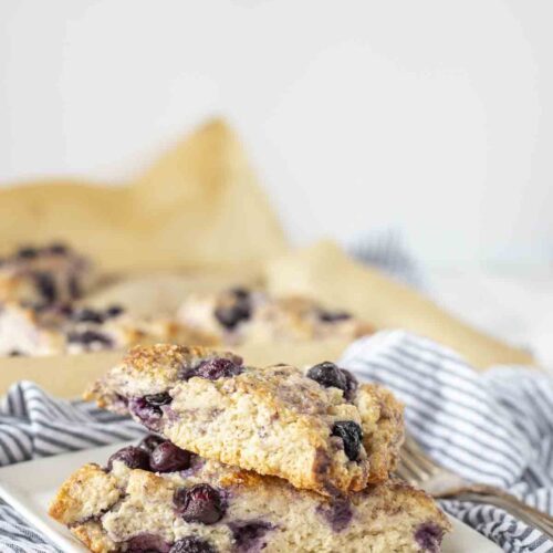 two blueberry sourdough scones stacked on white plate.