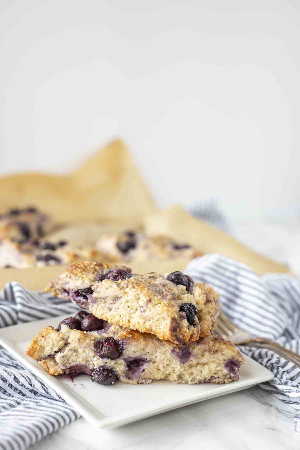 two blueberry sourdough scones stacked on white plate.