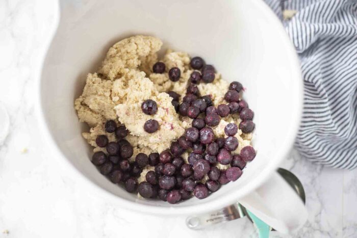 Folding Blueberry into dough in a white bowl.