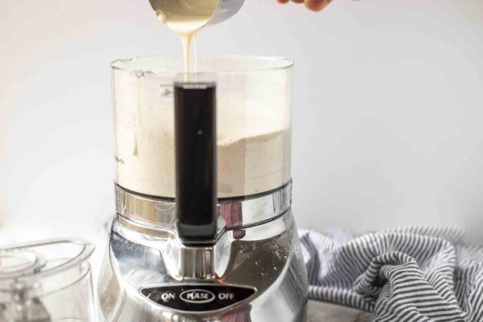 Adding sourdough starter to a food processor bowl with flour and butter.