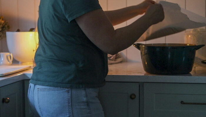 Placing bread dough on parchment paper into a cold dutch oven.