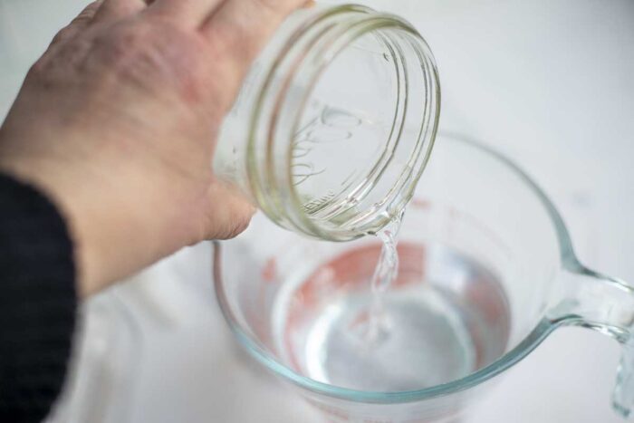 Pouring rubbing alcohol into a measuring cup with water and dish soap.