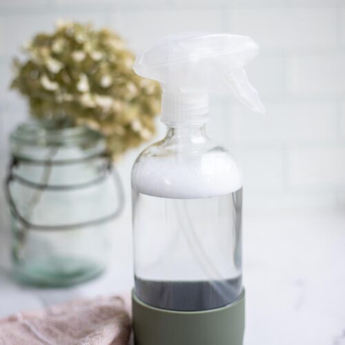 homemade granite cleaner in a spray bottle with a pink towel and a dried flowers in the background.