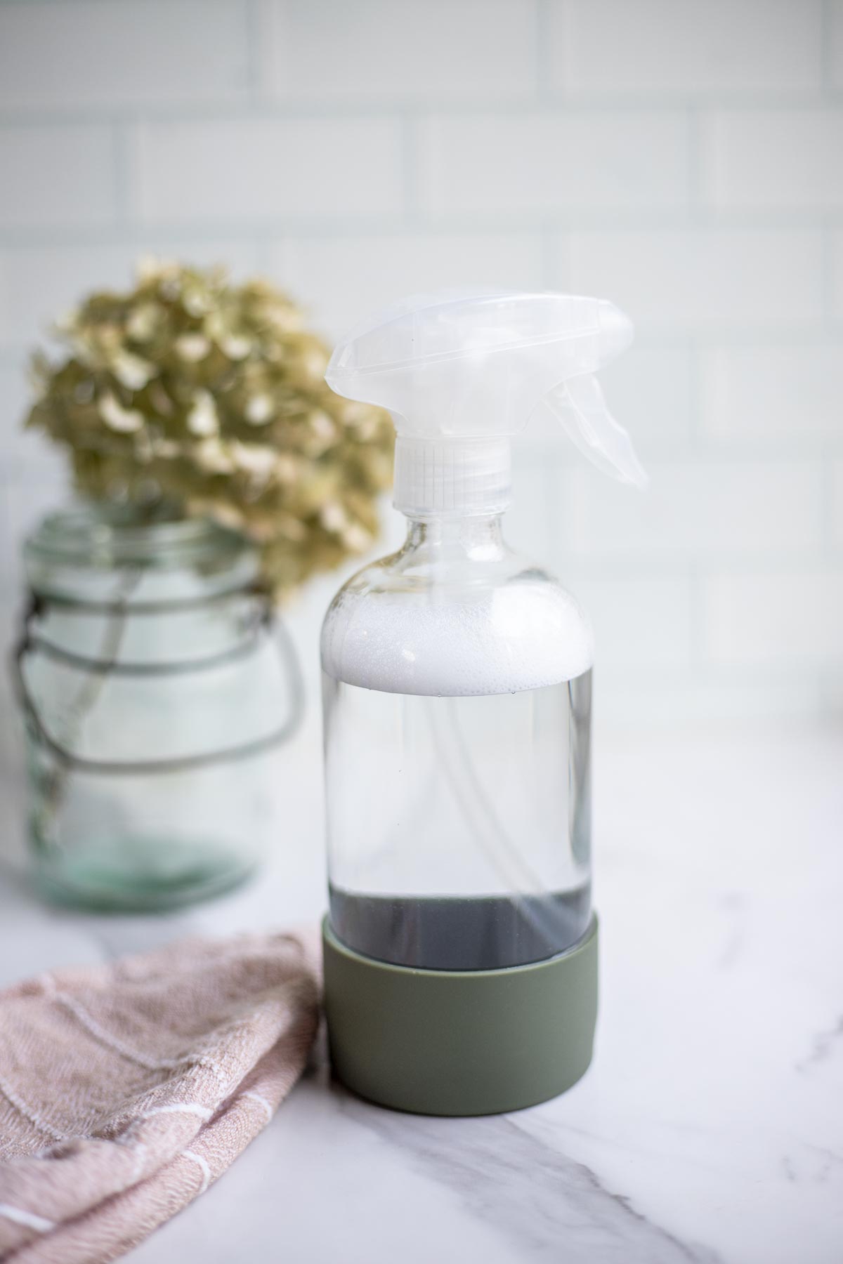 homemade granite cleaner in a spray bottle with a pink towel and a dried flowers in the background.