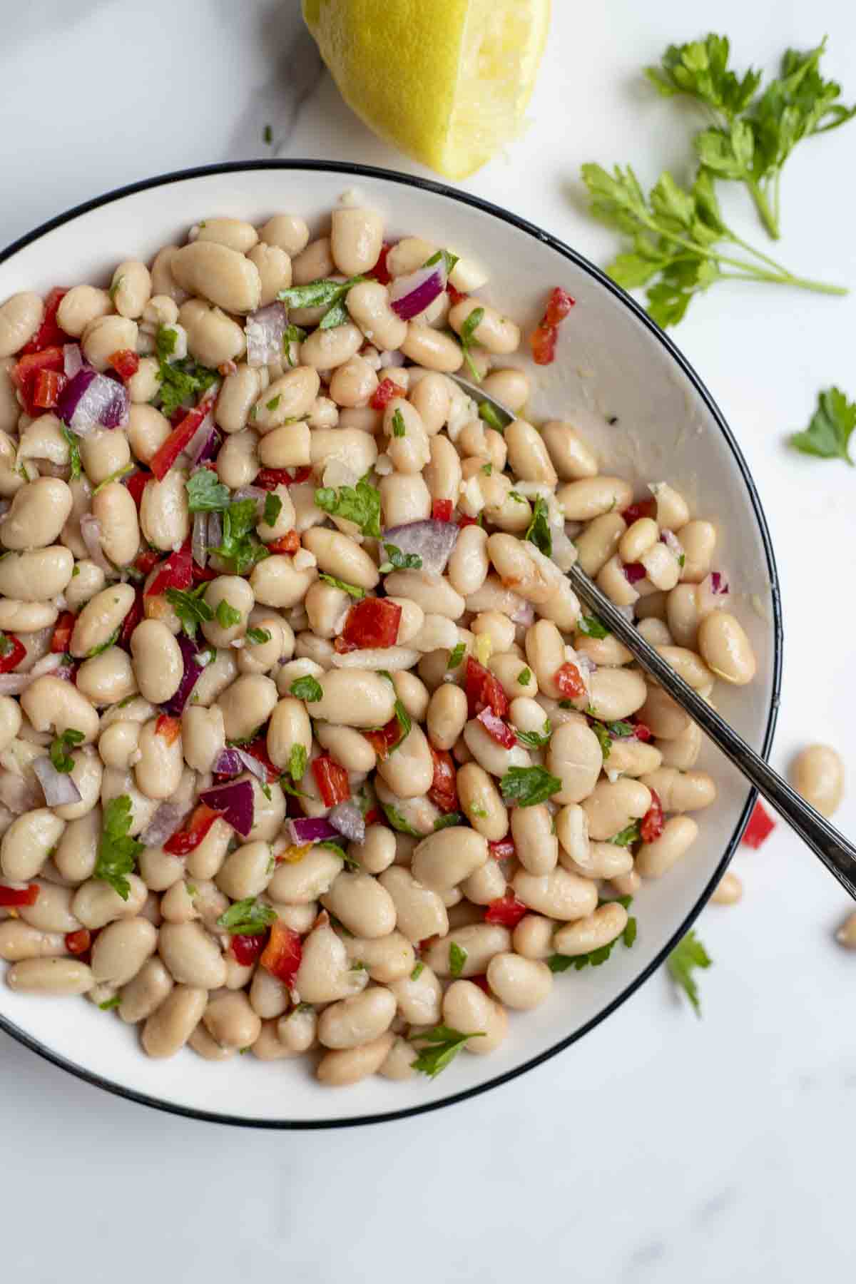 white bowl full of white bean salad with red pepper and fresh herbs.