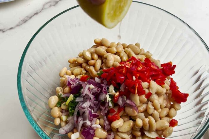 adding fresh lemon juice to a bowl of beans, onions, peppers, and herbs.