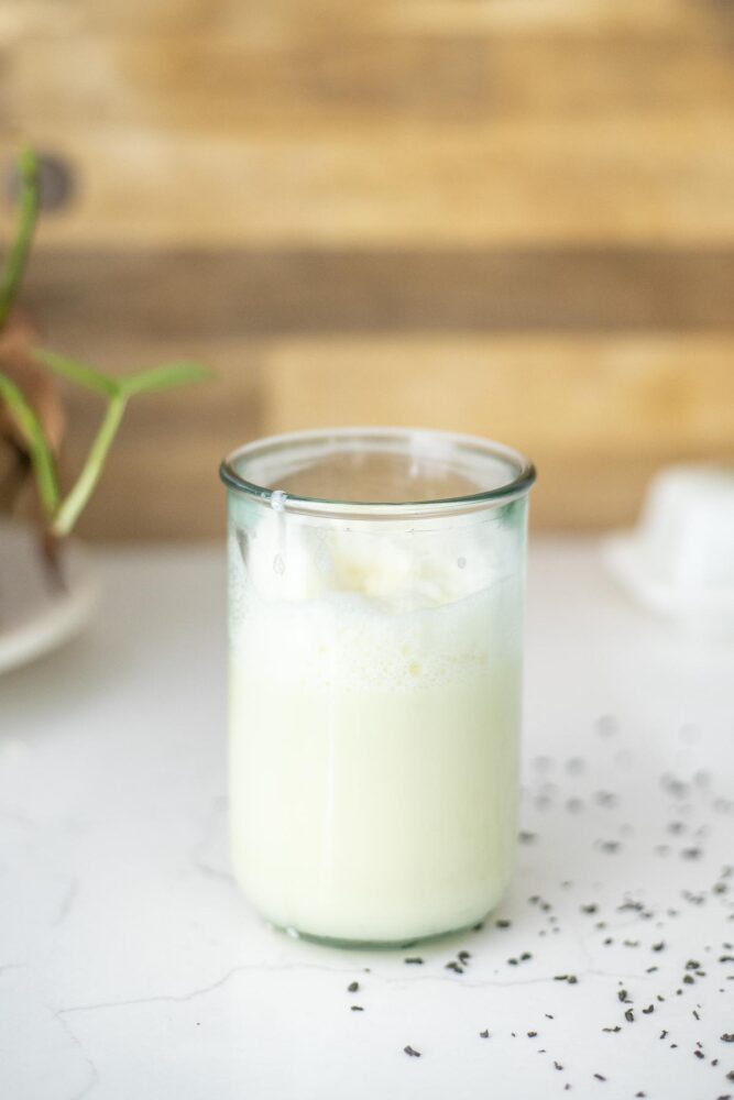 Green tea latte in a tall glass on a white countertop with green tea sprinkled around.