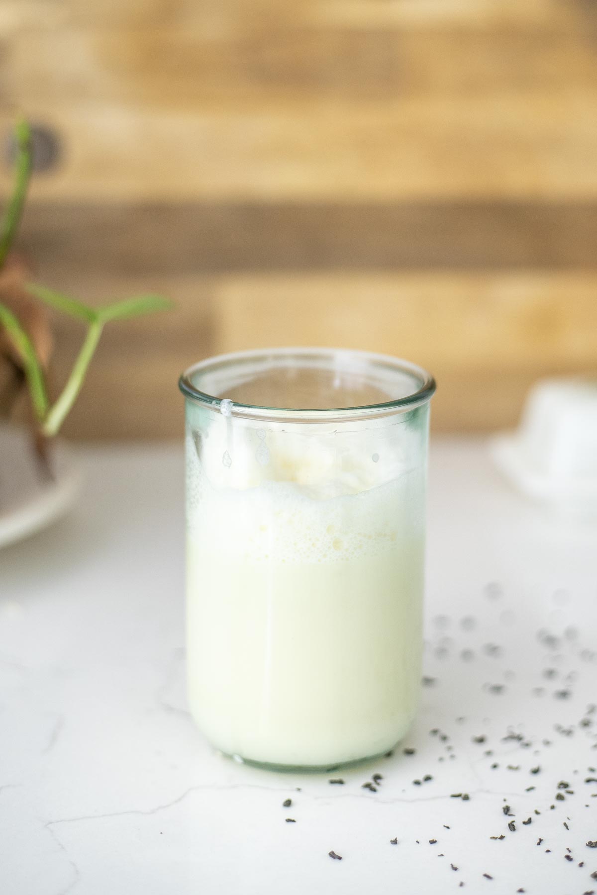 Green tea latte in a tall glass on a white countertop with green tea sprinkled around.