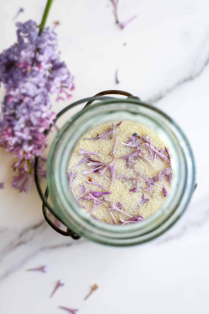 Lilac sugar with fresh lilac flowers in a jar on a countertop.