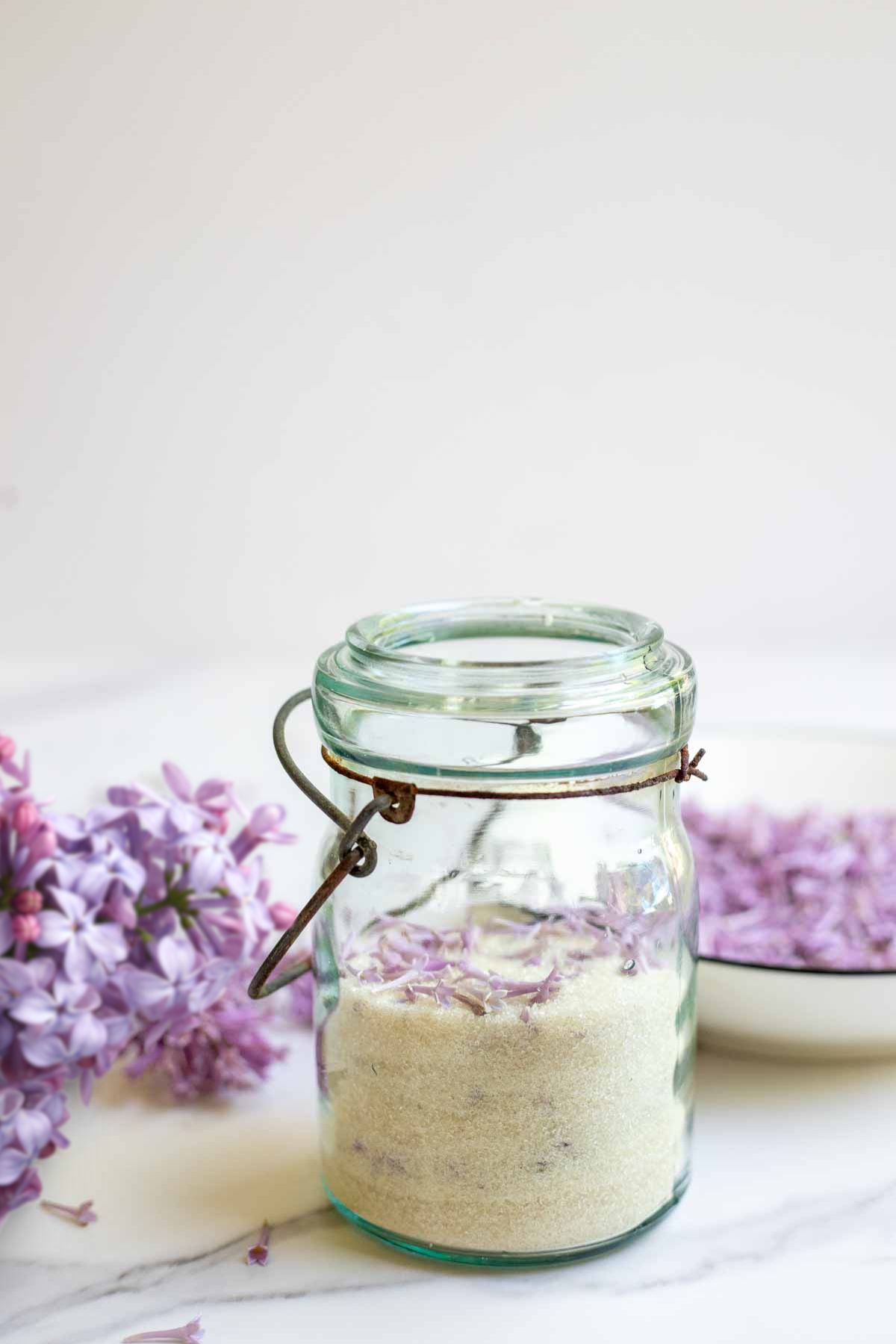 Lilac sugar in a antique mason jar with fresh lilac in the background.