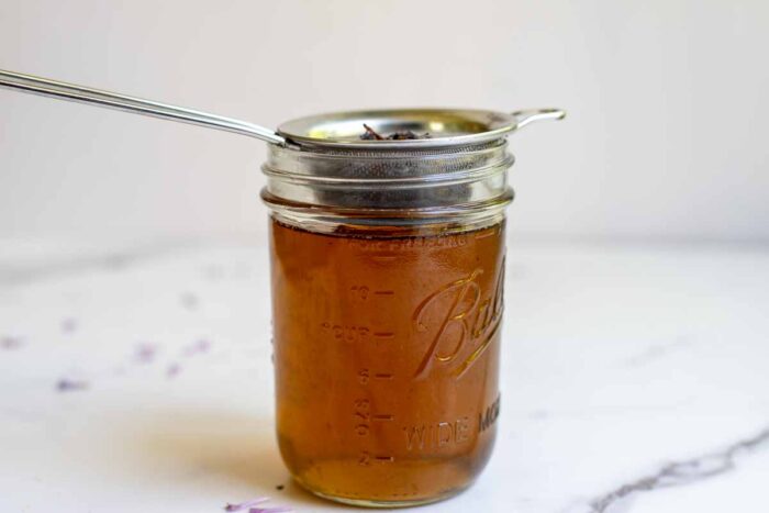 Straining lilac syrup into a mason jar on a countertop.
