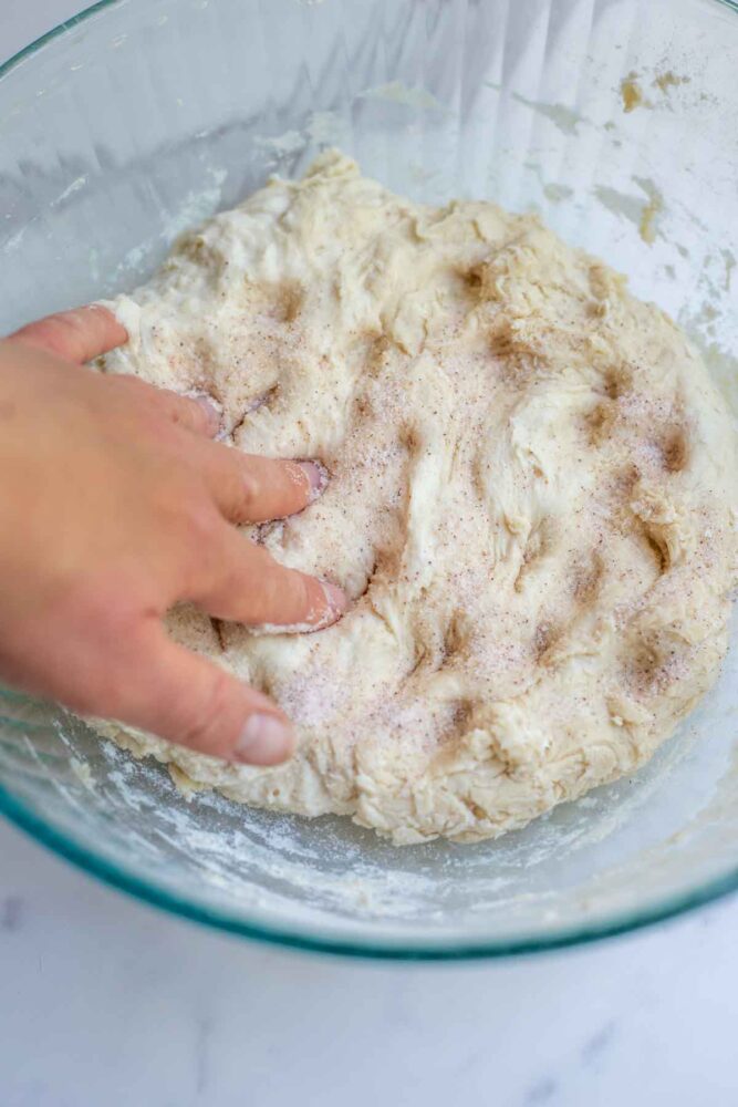 Dimpling in salt to sourdough bread dough in a glass bowl.