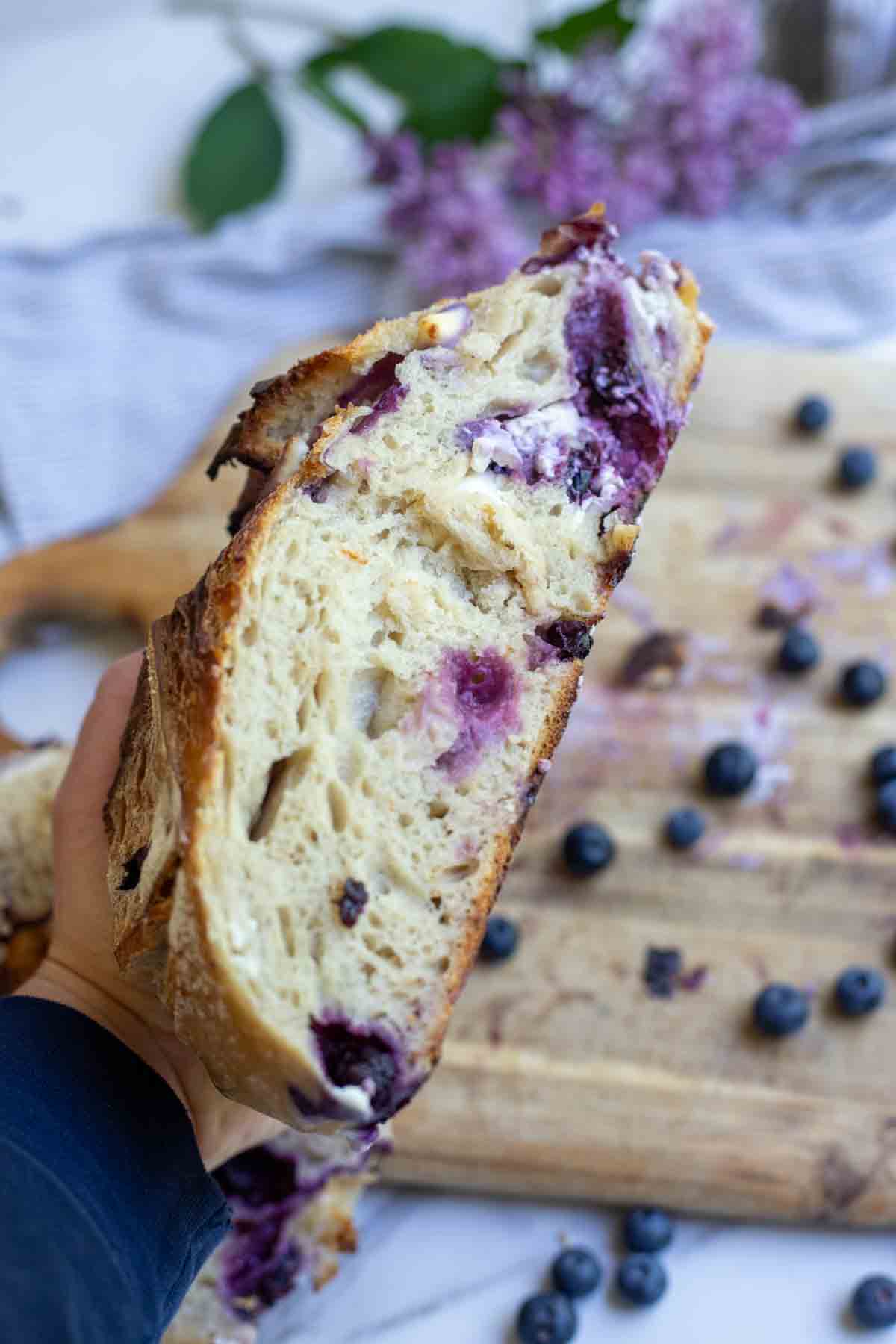 Hand holding a half of a loaf of sourdough blueberry bread.