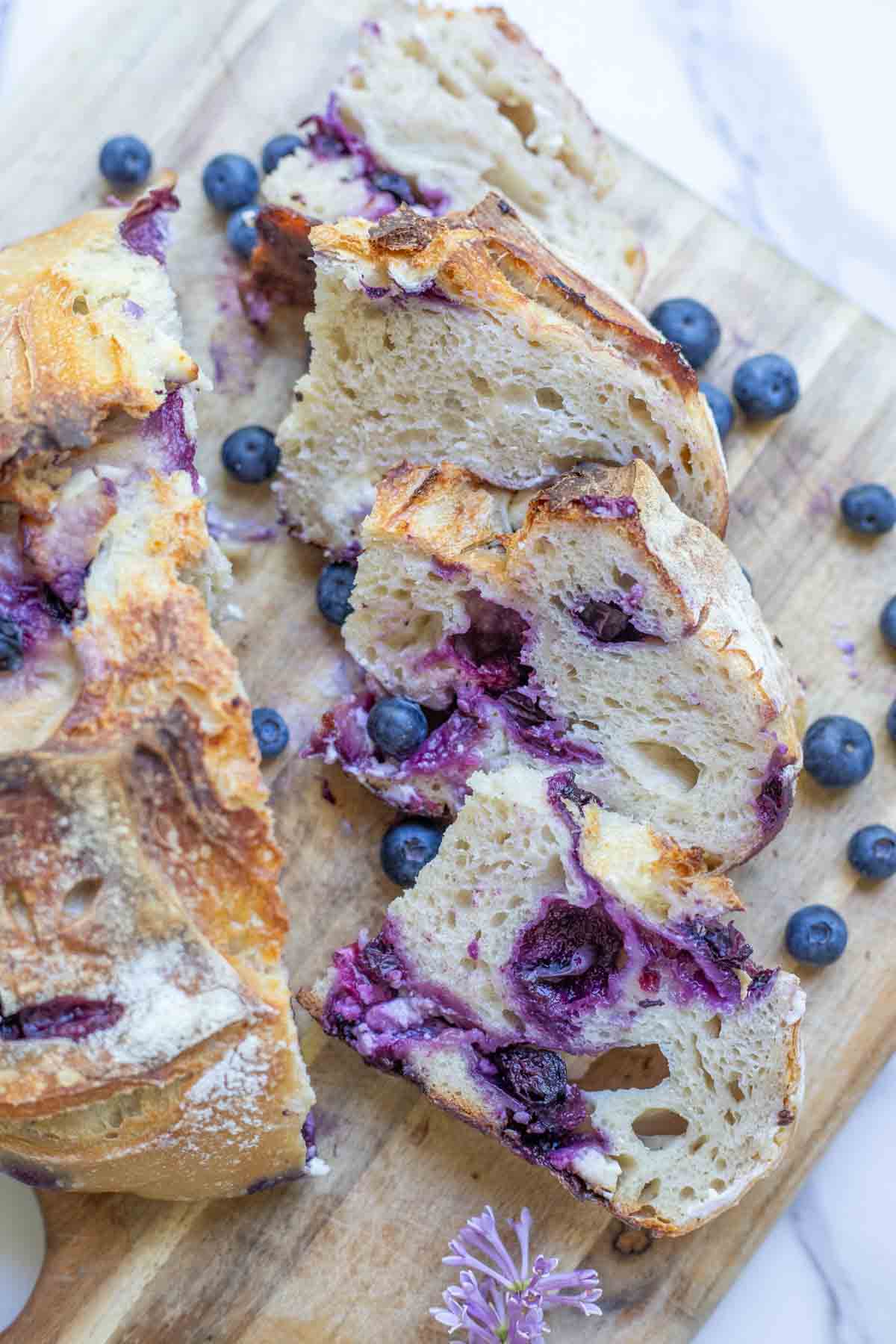 Sourdough blueberry cream cheese boule sliced on a wooden cutting board with fresh blueberries scattered.