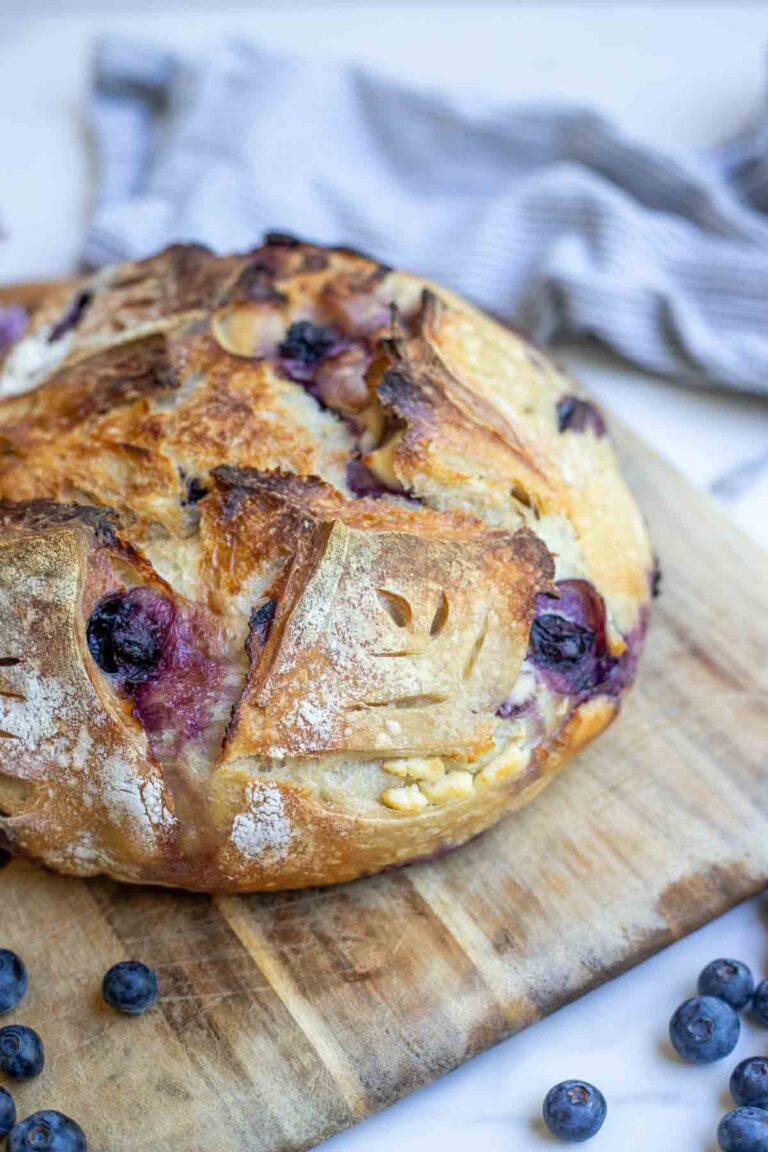 Sourdough blueberry and cream cheese bread on a cutting board surrounded by fresh blueberries.
